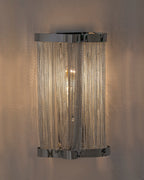 Skulpta Wall Sconce mounted on a wall, featuring a polished silver finish and cascading metal chain curtain that softly diffuses warm light, creating an elegant modern ambiance.