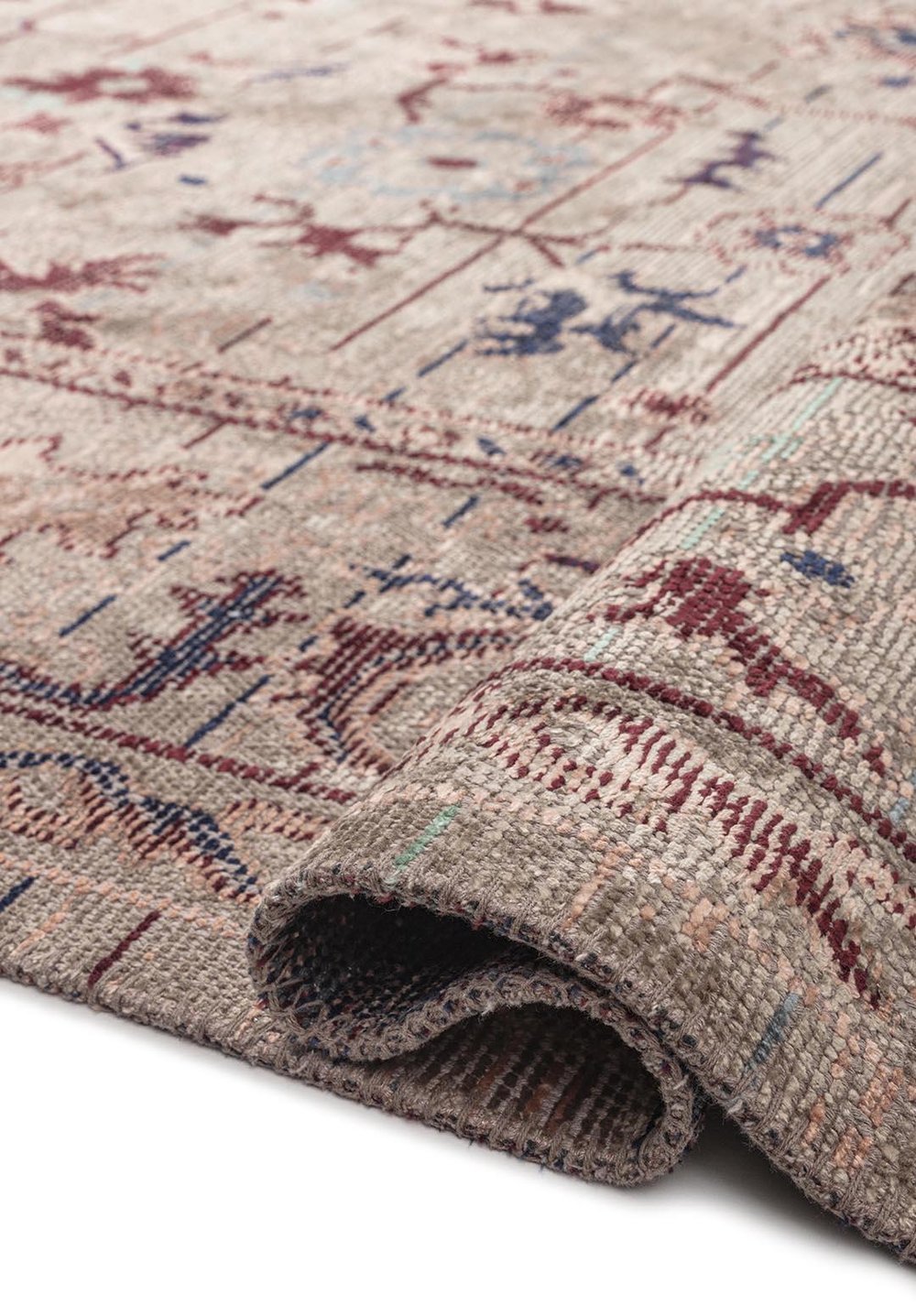 Folded corner detail of a traditional patterned rug with a textured weave in muted neutral and earthy colors.