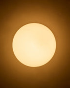 Round wall-mounted light with an opaque white glass shade emitting a warm, soft glow against the wall.