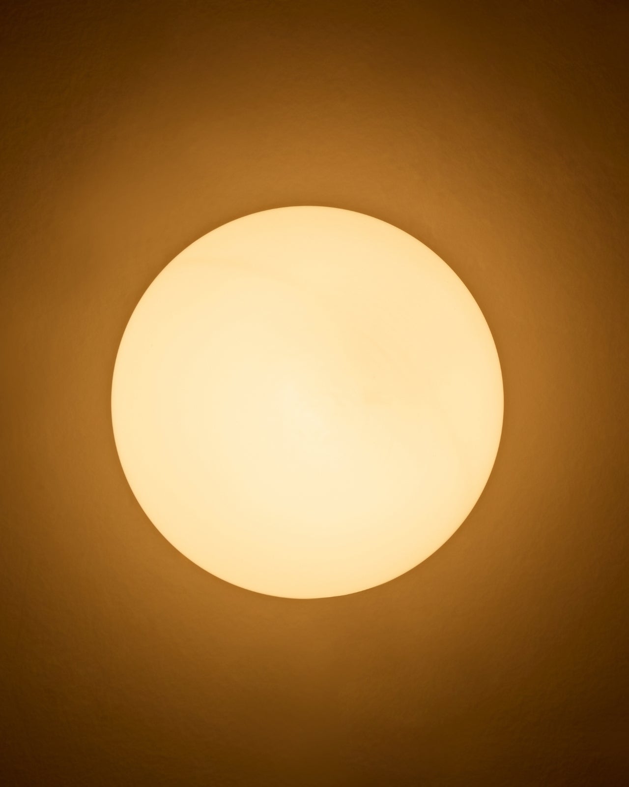 Round wall-mounted light with an opaque white glass shade emitting a warm, soft glow against the wall.