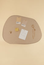 Asymmetrical fabric pinboard with a beige surface and outer frame, displaying pinned Pantone cards, notes, and jewelry against a soft neutral background.