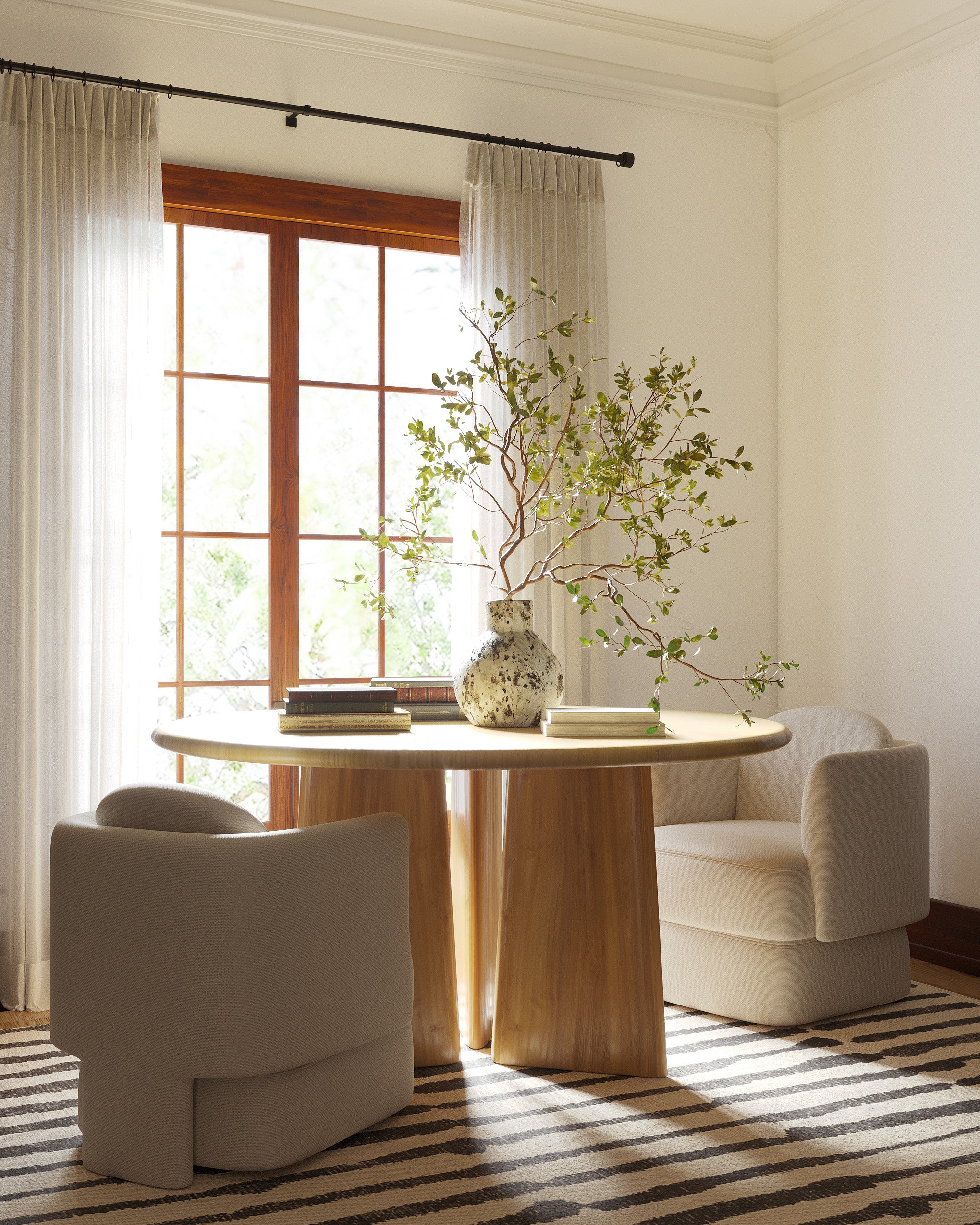 Sunlit dining area with a round wooden table, upholstered chairs, and a striped rug beneath.