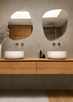Bathroom vanity with two round sinks, wooden cabinets, and two oval mirrors on a beige wall.