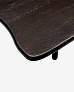 Close-up detail of a dark brown wooden table corner with a smooth curved edge and a small black leg, shown against a light gray background.