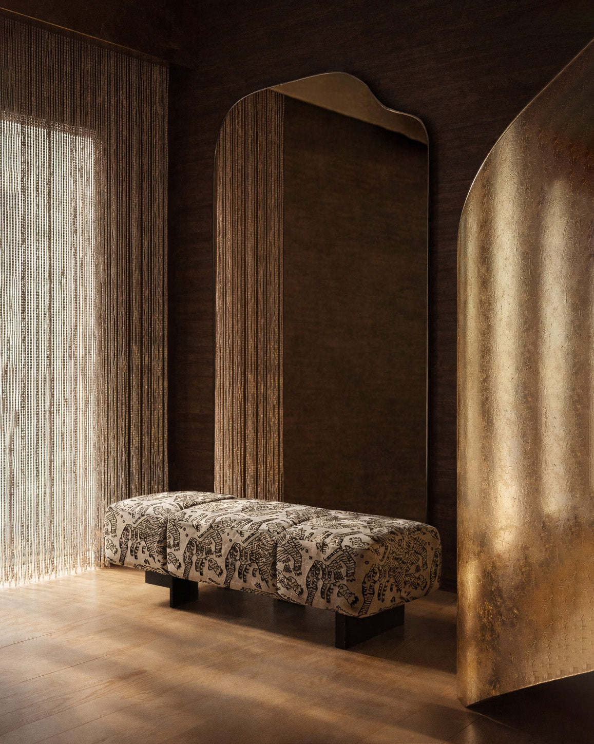 Warm, moody interior with an irregular full length mirror, patterned upholstered bench, textured drapery, and a curved metallic accent panel.