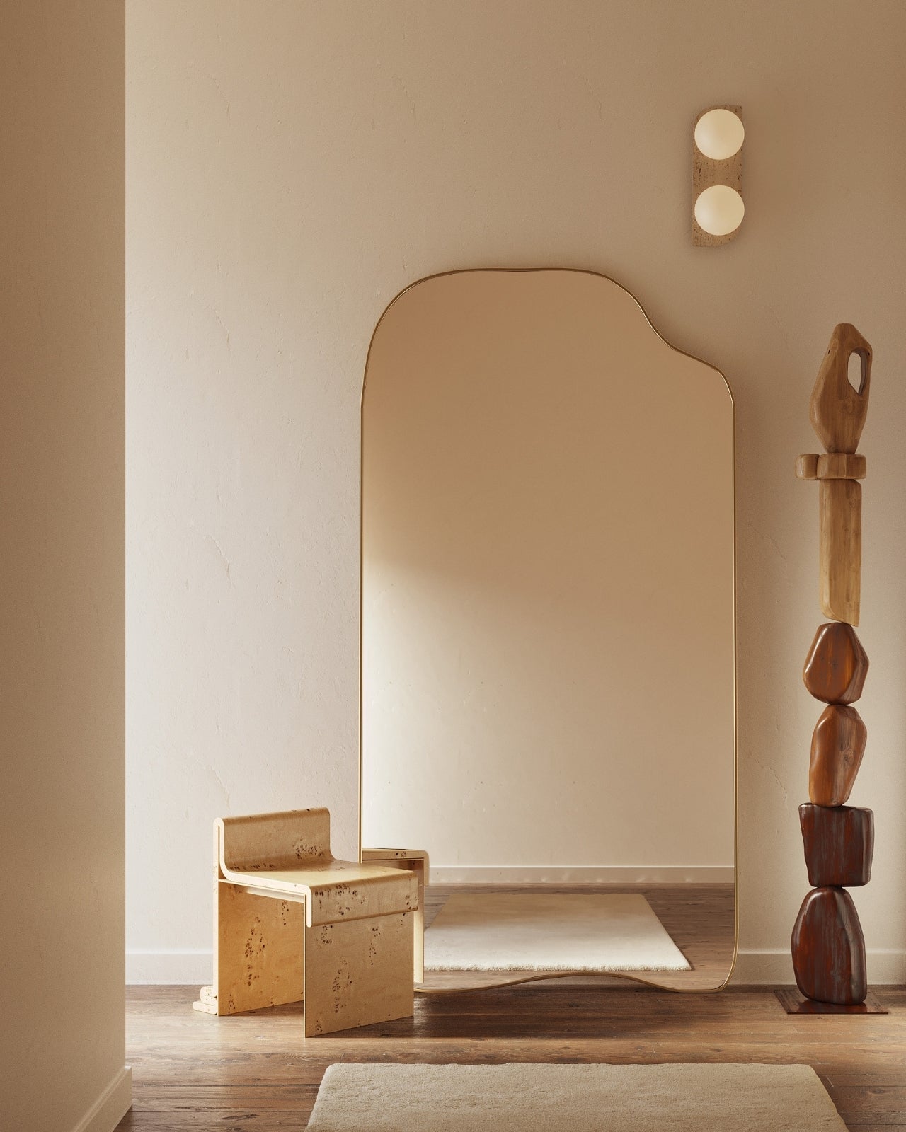 Minimal interior with a large irregular full length mirror, light wood chair, sculptural wooden totem, and warm neutral walls.