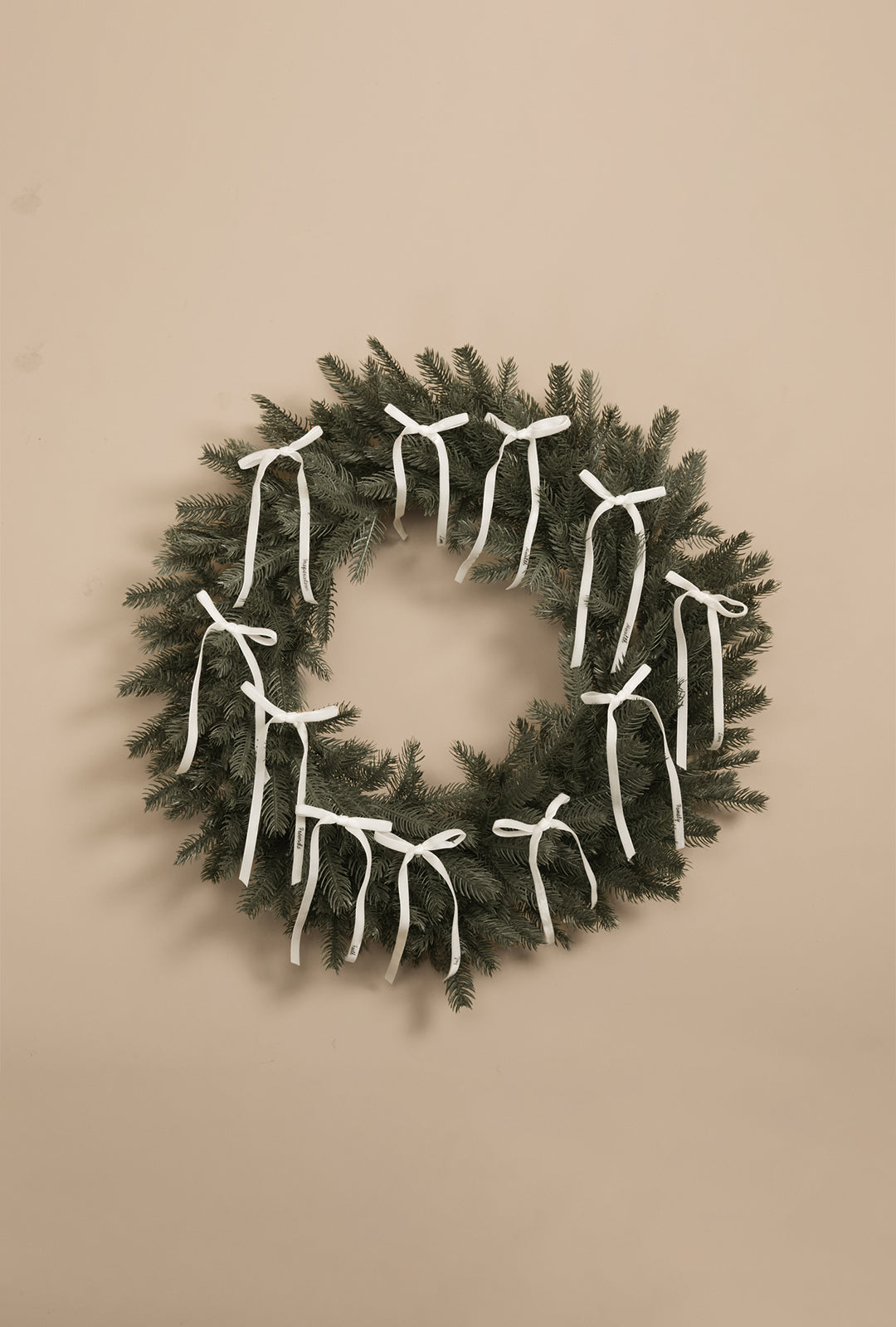 Green artificial wreath decorated with eleven white velvet ribbon bows, displayed on a neutral background.