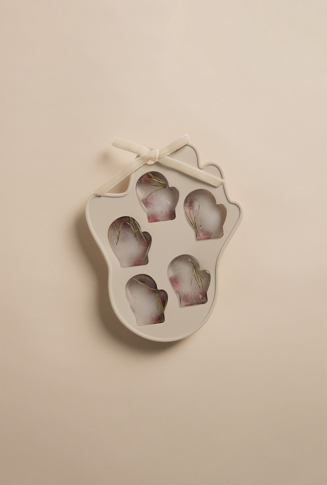 A beige, mitten-shaped silicone mold with five mitten cavities, tied with a small bow, shown with frozen shapes inside on a neutral background.