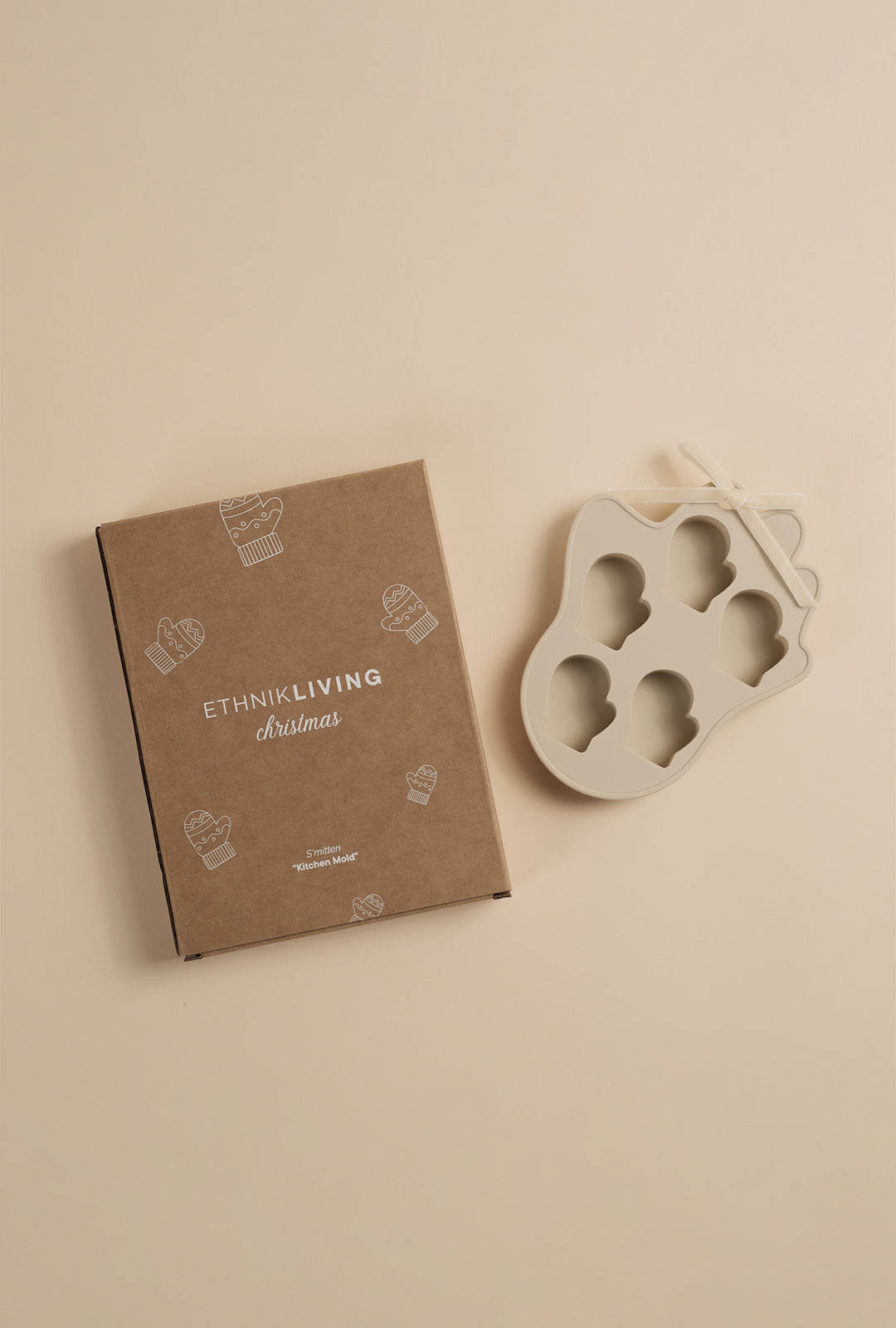 Top view of a beige mitten-shaped silicone kitchen mold placed beside its Ethnik Living Christmas branded cardboard box.