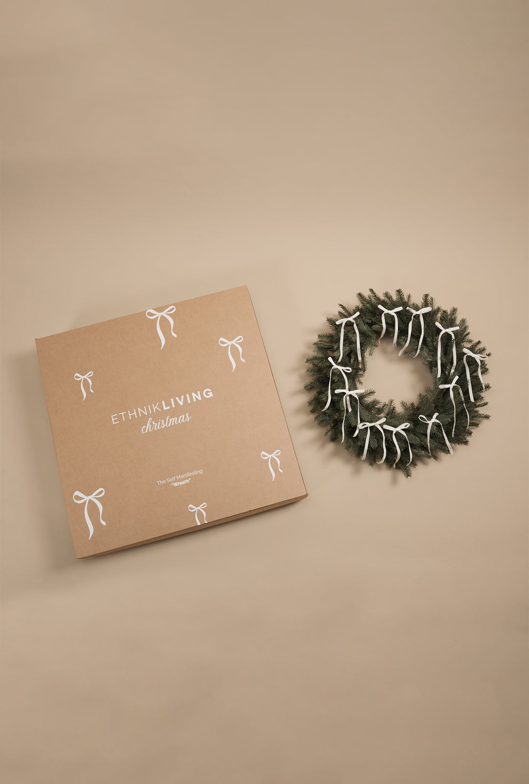 Green decorative wreath with white ribbon bows displayed next to a branded gift box on a neutral background.