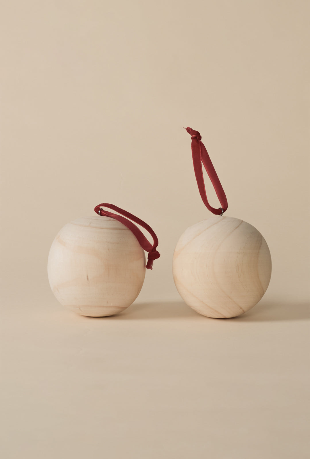 Two unfinished wooden ball ornaments with red hanging loops, made from natural pine wood.