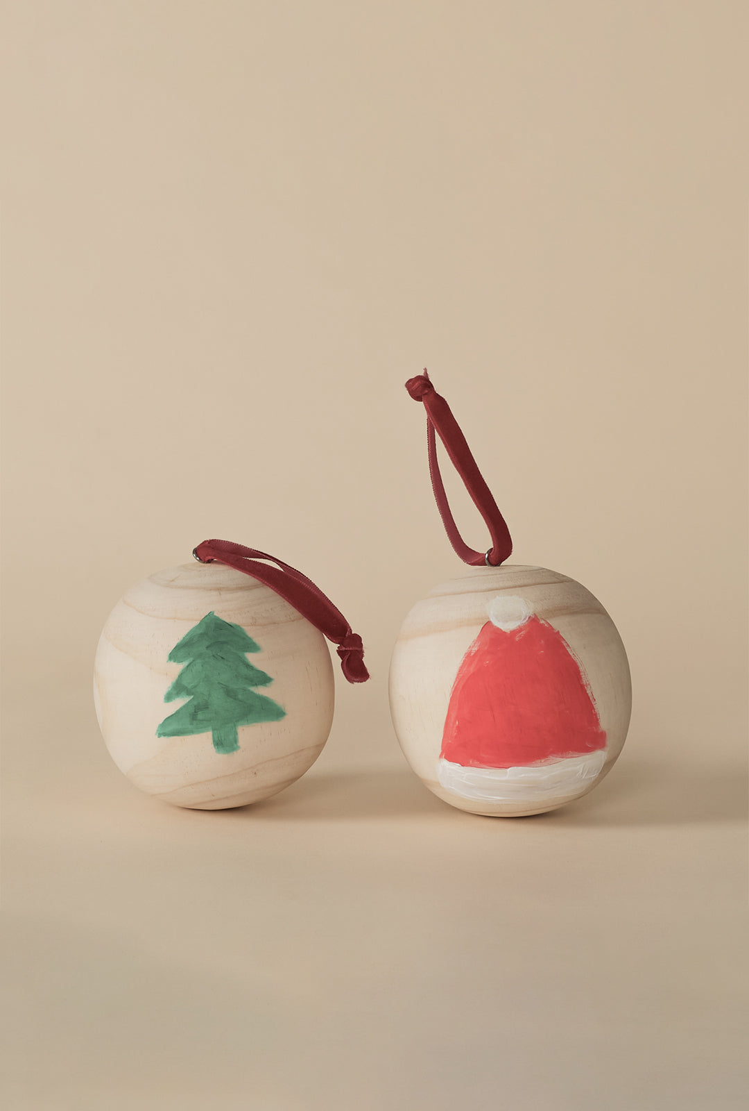 Two hand-painted wooden ball ornaments, one with a green Christmas tree and one with a red Santa hat, each with a red hanging loop.