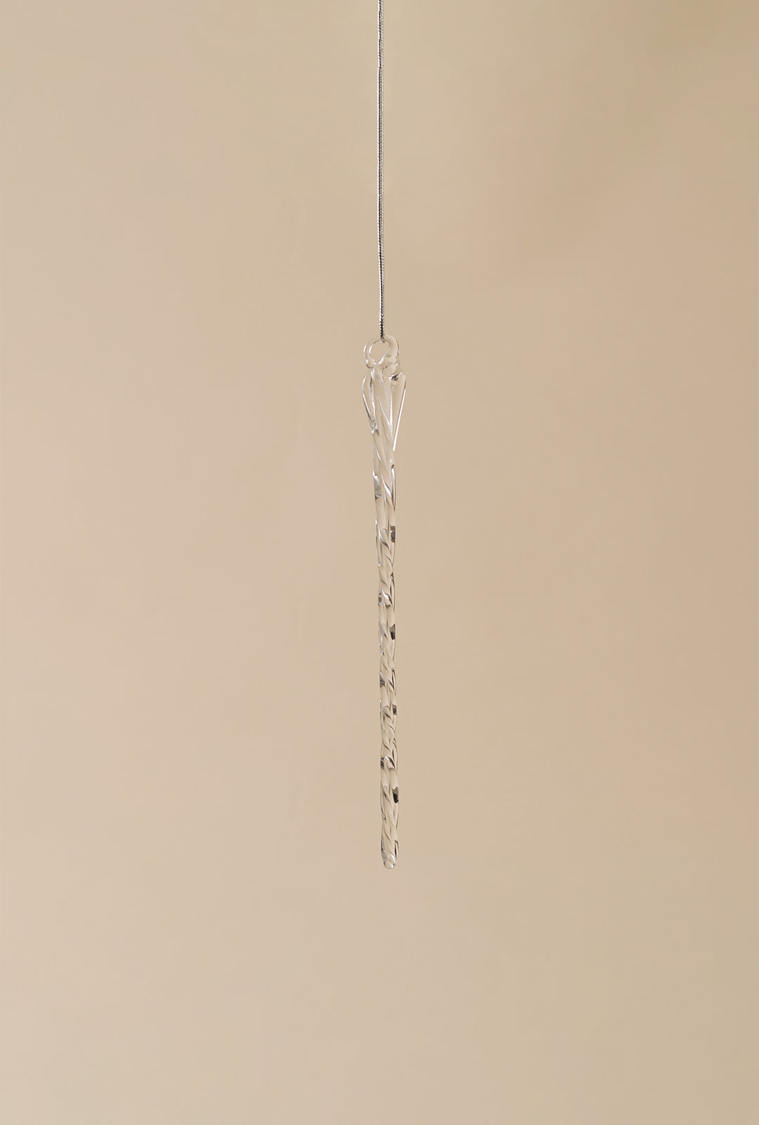 A single clear glass icicle ornament hanging from a thin loop against a neutral background.