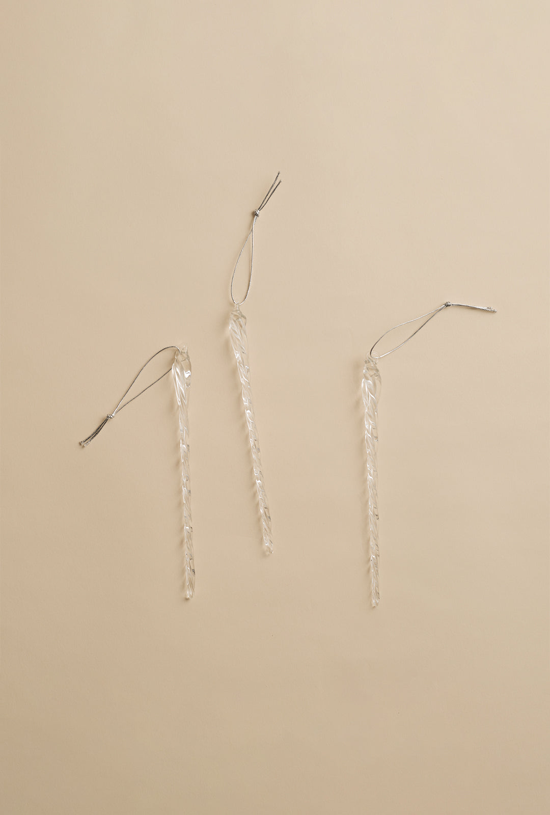 Three clear glass icicle ornaments with hanging loops arranged on a neutral background.