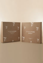 Two Ethnik Living Christmas wreath packaging boxes displayed side by side, made of kraft paper with white bow illustrations and branded text on the front.