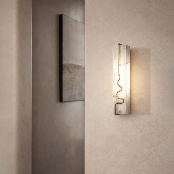 Alabaster wall sconce with brass detail casting warm light on a textured wall.