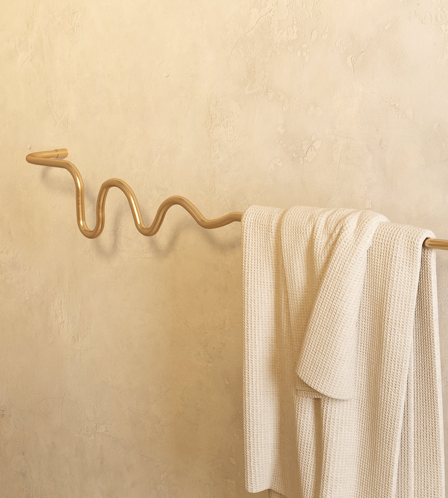 Brass wavy towel bar holding a textured white towel against a light, textured wall.