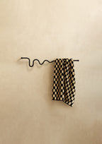 Black wavy towel bar holding a checkered towel, shown against a neutral textured wall.