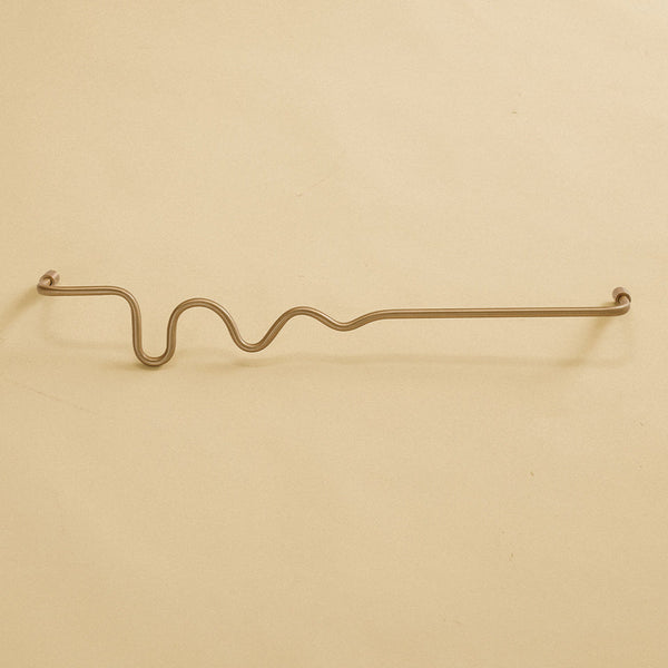 Brass-colored towel bar with a wavy organic shape, shown in a studio setting on a neutral background.
