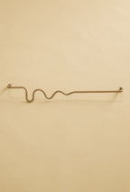 Brass-colored towel bar with a wavy organic shape, shown in a studio setting on a neutral background.