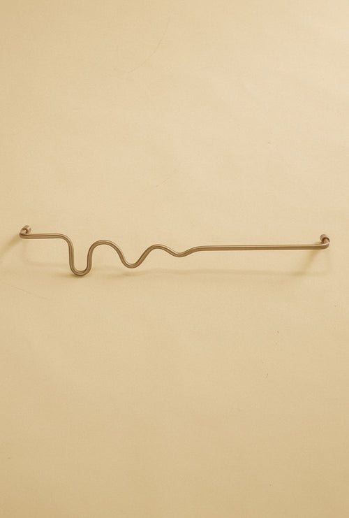 Brass-colored towel bar with a wavy organic shape, shown in a studio setting on a neutral background.