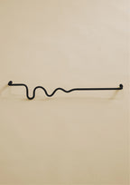 Black-colored towel bar with a wavy organic shape, shown in a studio setting on a neutral background.