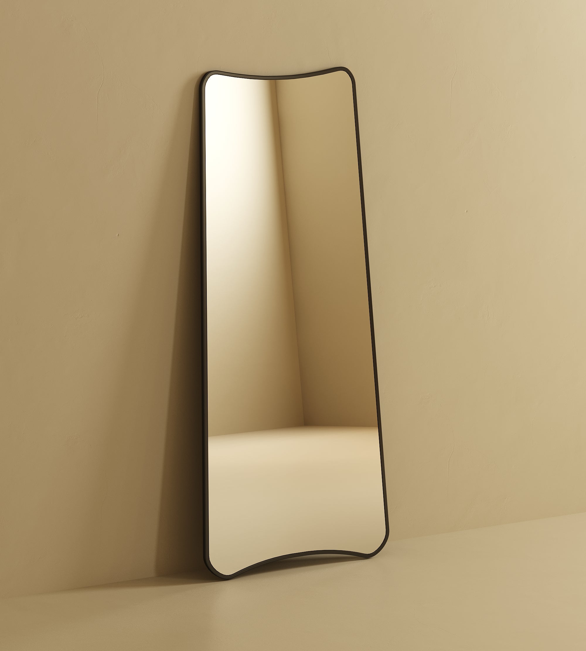 Tall full-length mirror with softly curved edges leaning against a wall, reflecting a minimal interior corner.