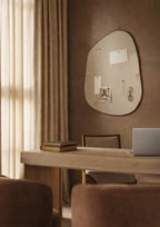 Asymmetrical fabric-covered pinboard with a brown outer frame, mounted on a warm-toned wall above a wooden desk, displaying pinned notes and photographs.