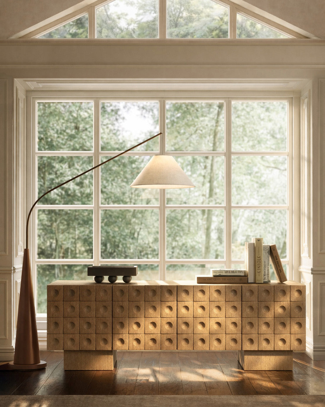Textured wooden sideboard styled in front of large windows with books and a sculptural floor lamp.