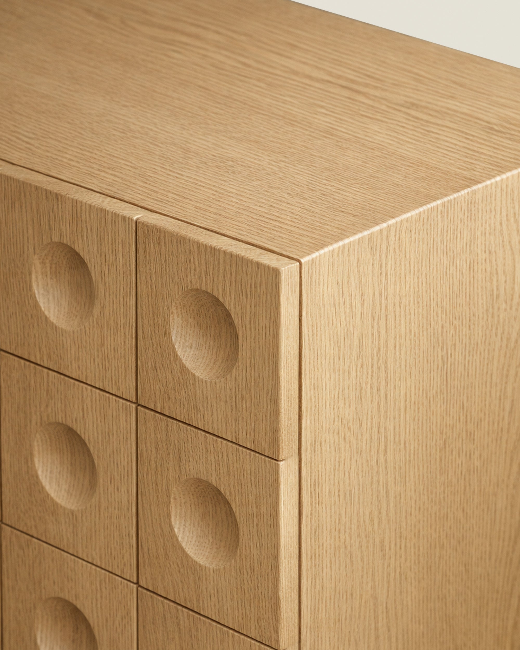 Close-up of a wood sideboard corner with circular indented drawer fronts and natural grain detail.