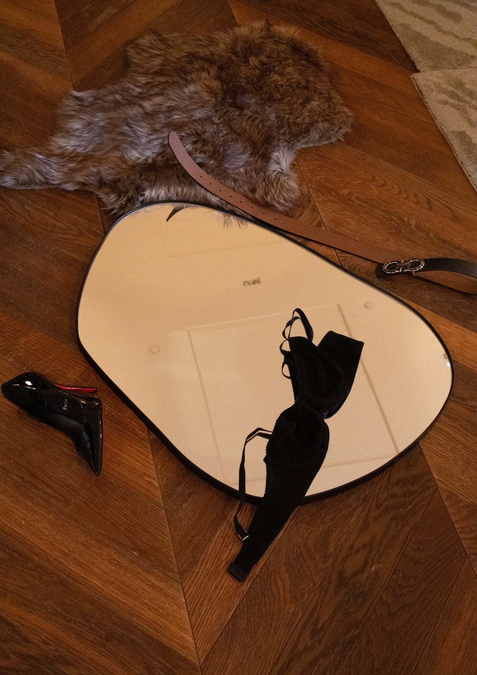 Mirror on a wooden floor with a shoe, belt, and fur rug nearby.