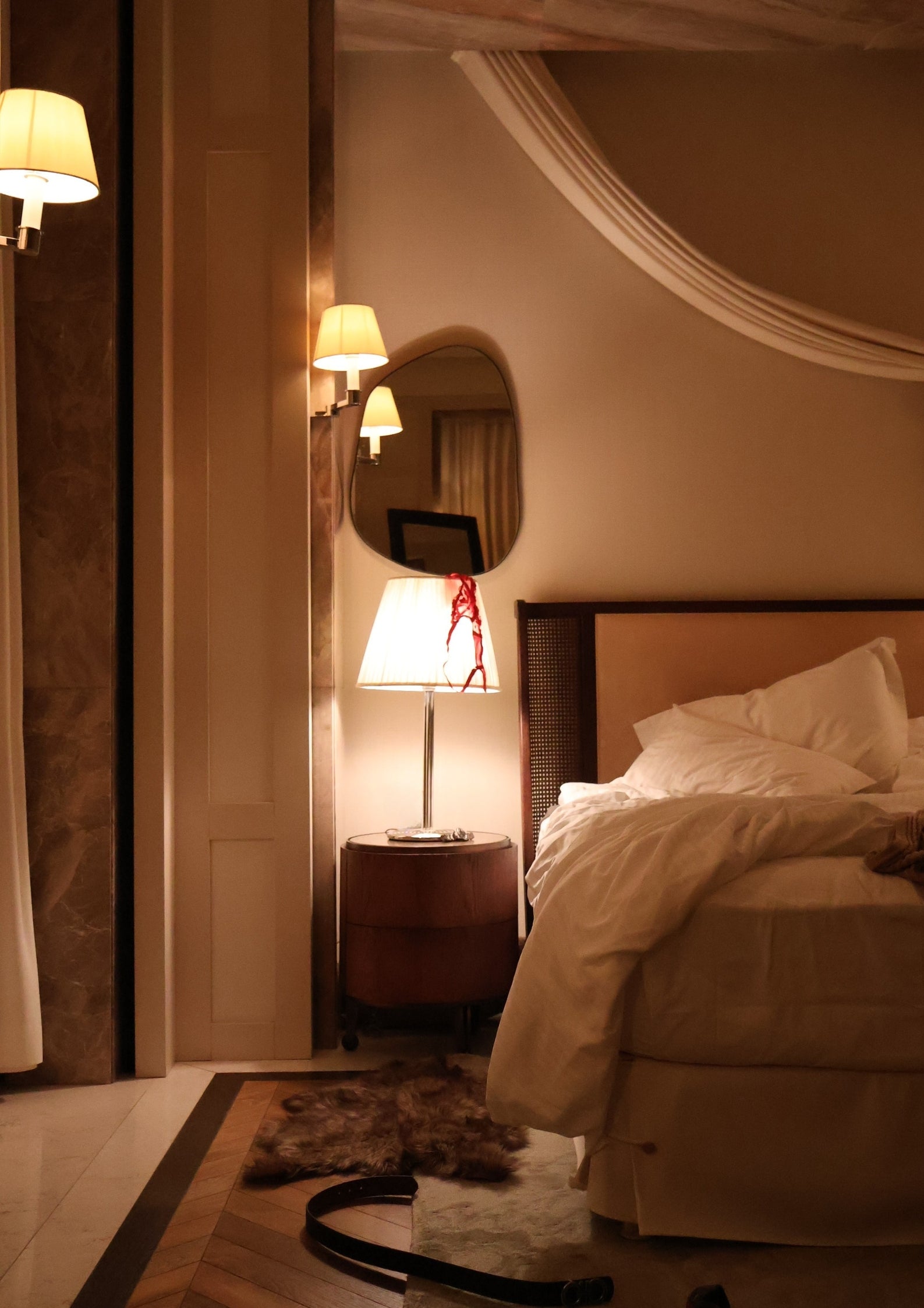 Bedroom scene with a bed, bedside lamp, wall mirror and fur rug on the floor.