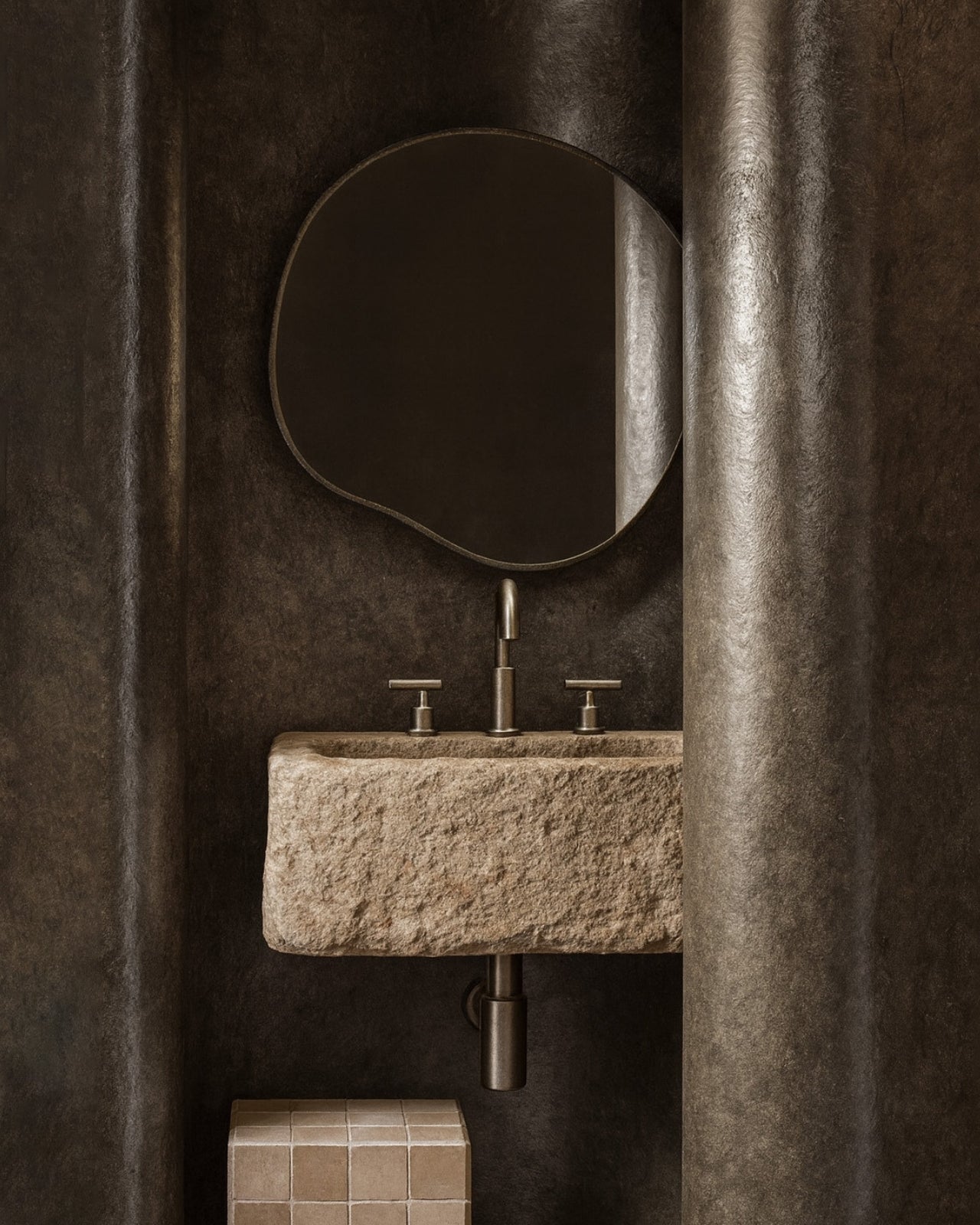 Organic-shaped wall mirror with a slim stainless steel frame mounted above a stone sink in a textured bathroom interior.