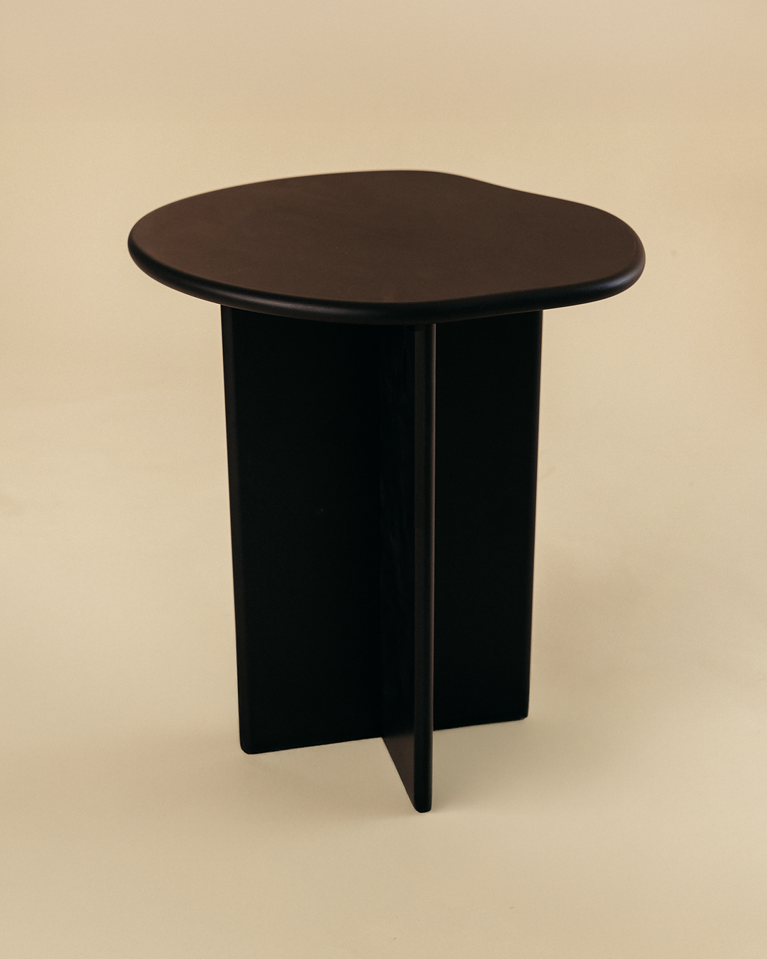 A minimalist black side table with a round tabletop and three vertical legs, shown from a slightly elevated angle against a neutral studio background.