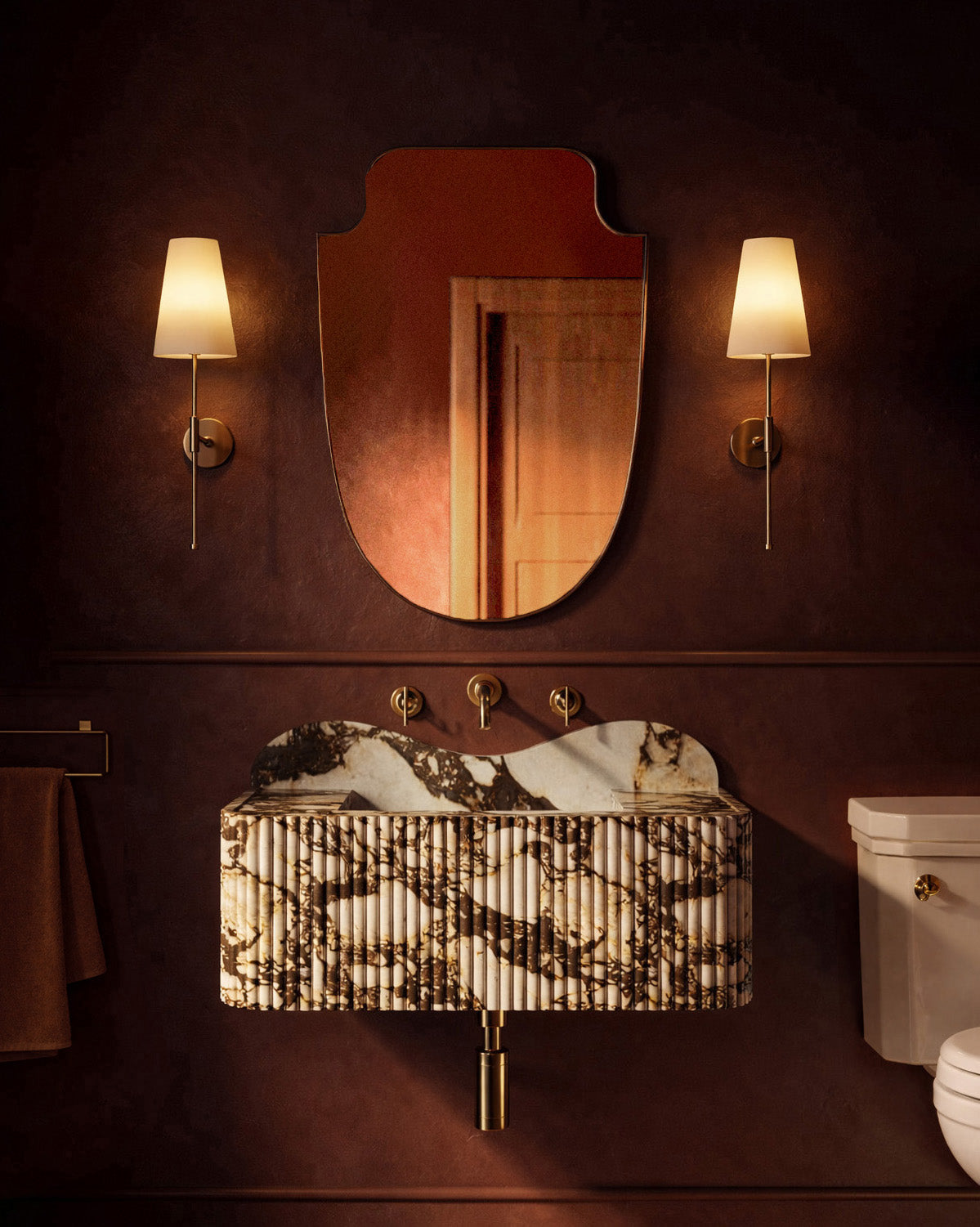 Moody bathroom with a sculpted wall mirror, brass sconces, and a marble pedestal sink against deep red walls.