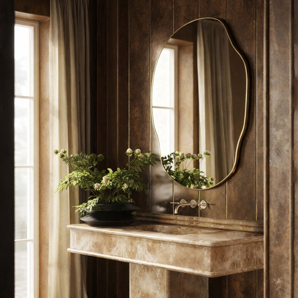 Asymmetrical brass-framed wall mirror installed above a stone console vanity.