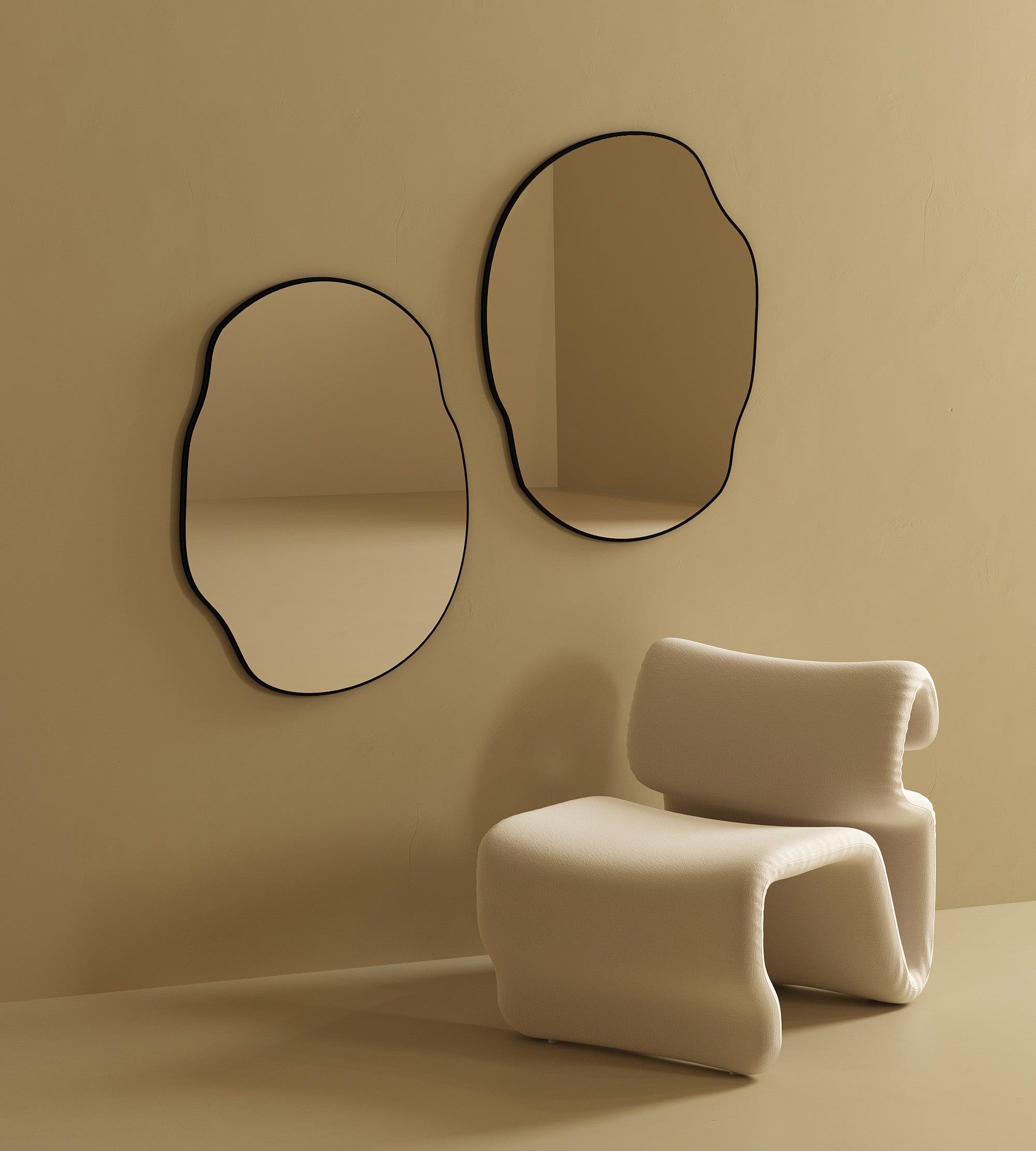 Two irregular-shaped wall mirrors with black frames mounted side by side on a beige wall above a sculptural upholstered chair.