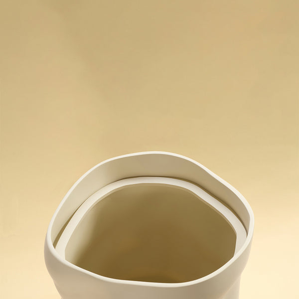 An open beige sculptural dustbin shown from above, highlighting the rounded rim and interior, against a light yellow background.