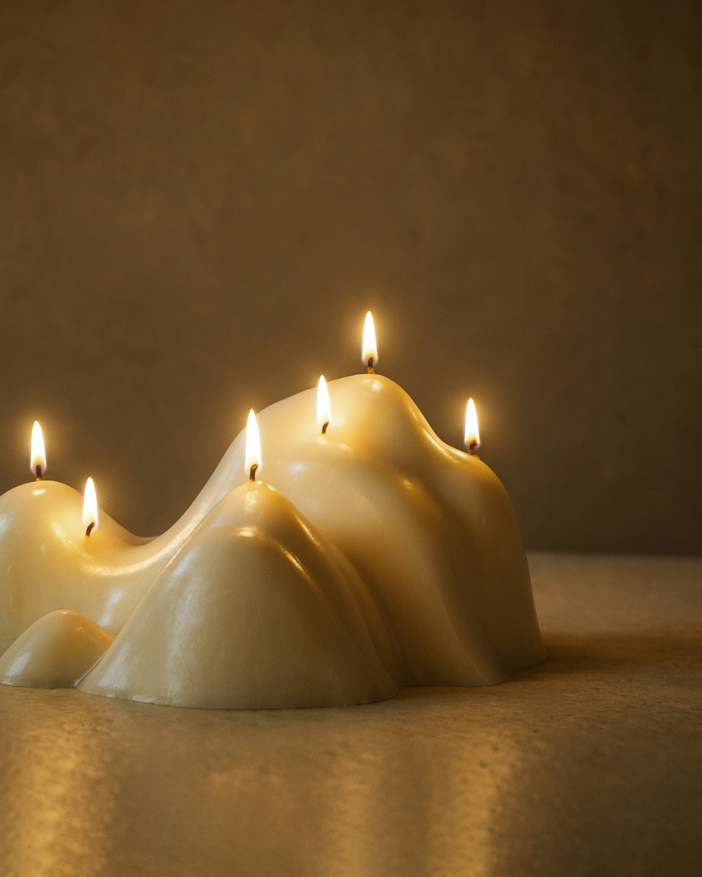 White sculptural candle with an organic, mountain-like shape and multiple lit wicks placed on a flat surface.