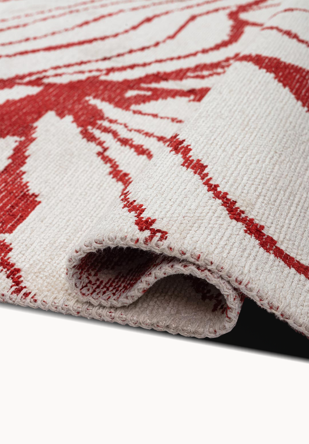 Close-up of a flat-woven rug corner showing folded edge, low-profile weave, and red abstract lines on a cream background.