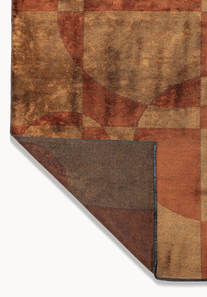 Corner detail showing a flat-woven texture with warm caramel and brown geometric patterns and a neatly finished folded edge.