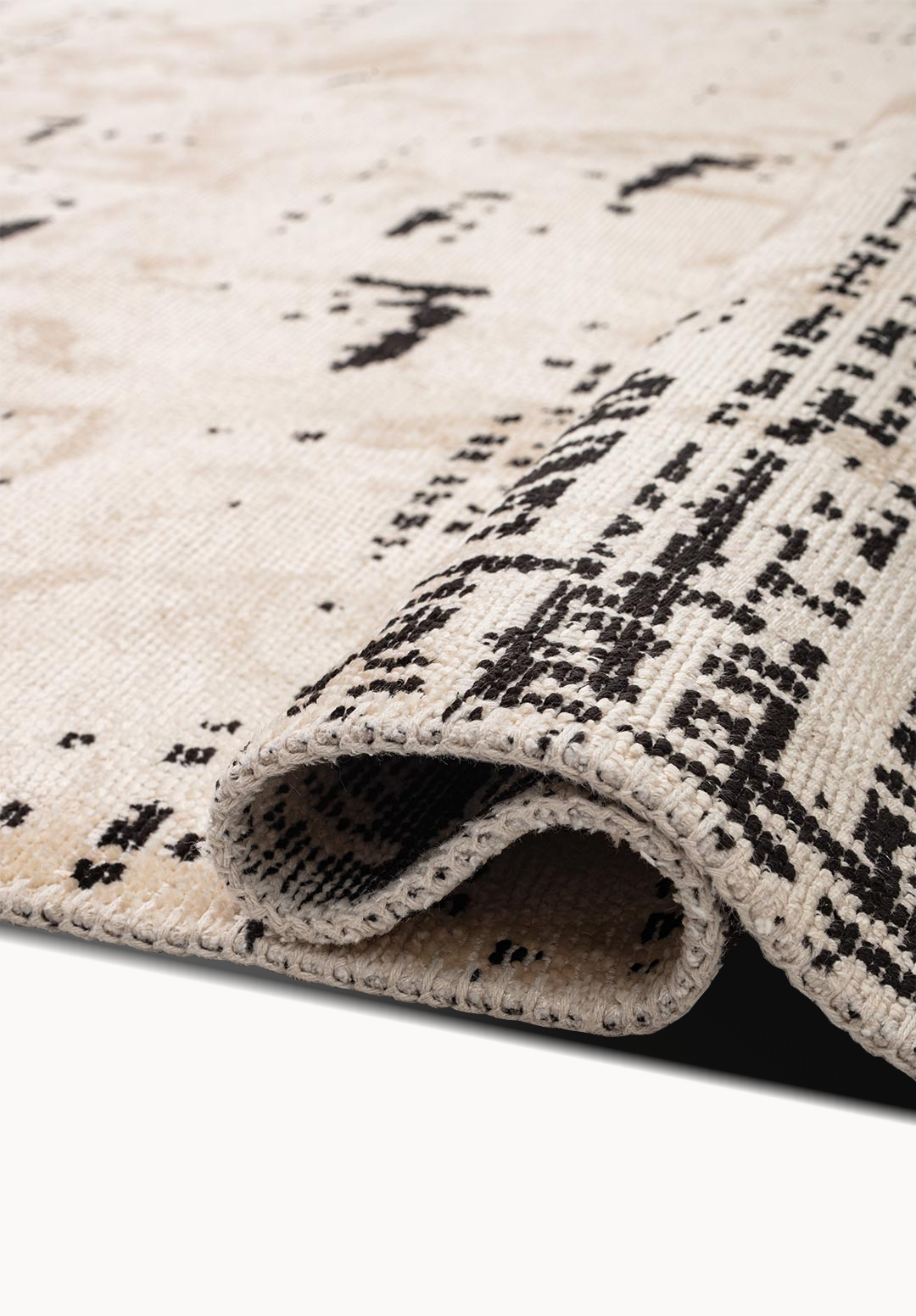 Detail view of a flat-woven rug corner with beige fabric and black abstract markings.